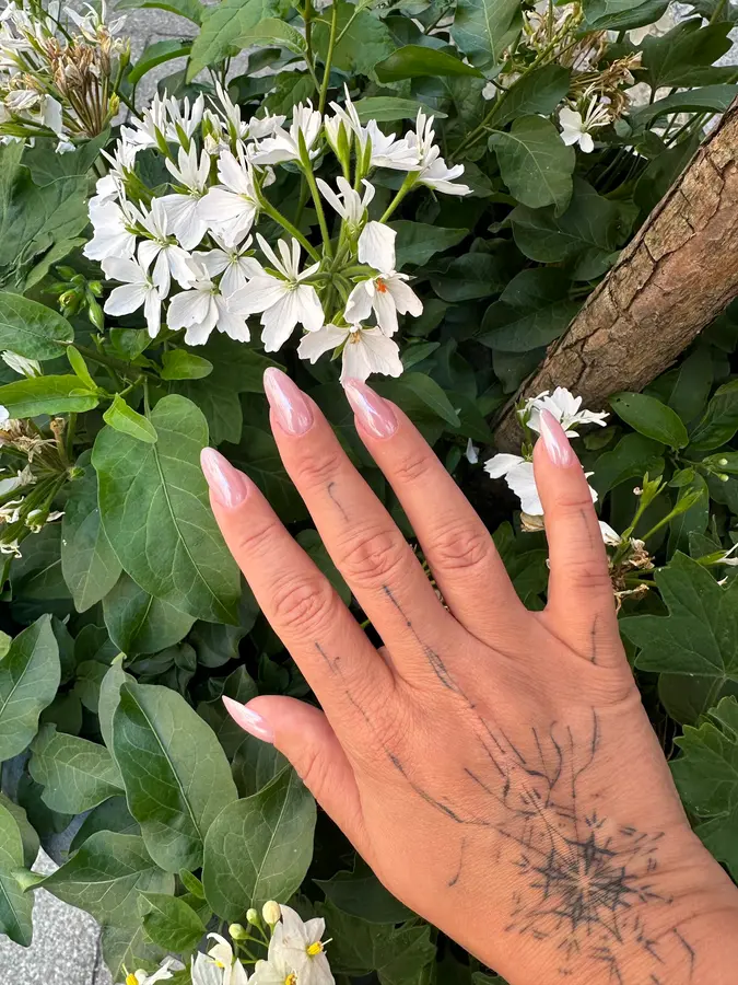Zartrosa Nägel vor weißen Blüten